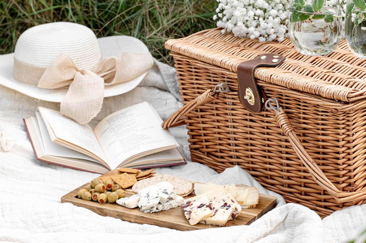 picnic basket and cheese board on a blanket