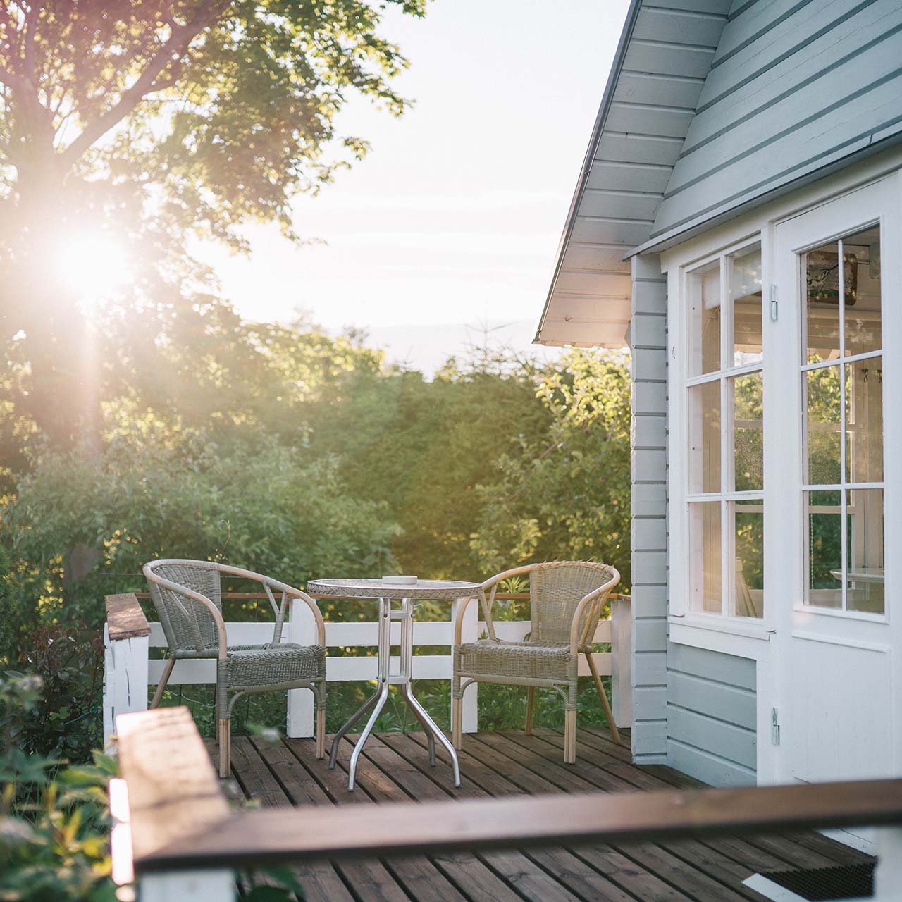 terrace of a blue coloured cottage with the sun shine through the trees