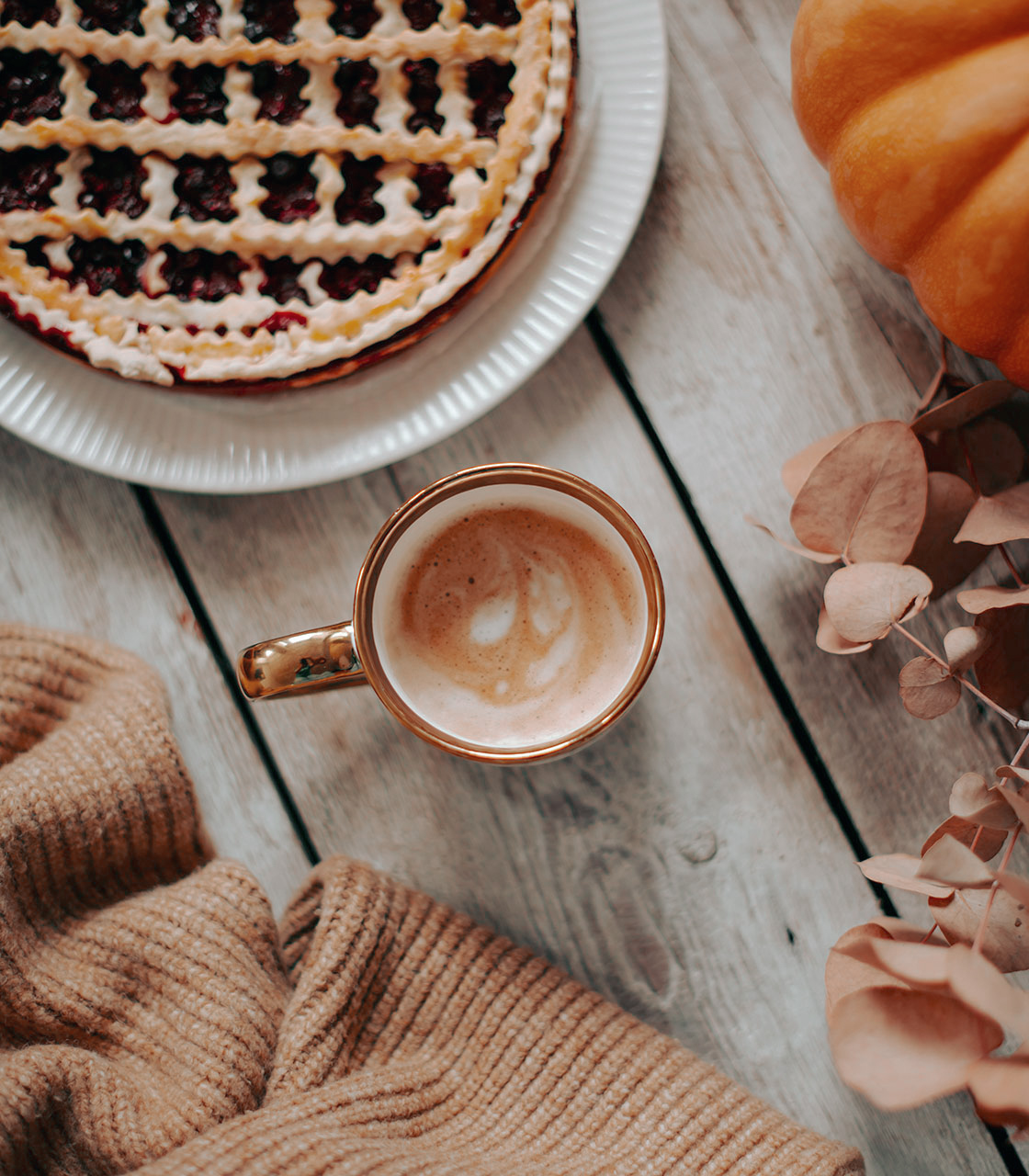 herfst flatlay met een kop koffie, taart, wolkentrui en een pompoen