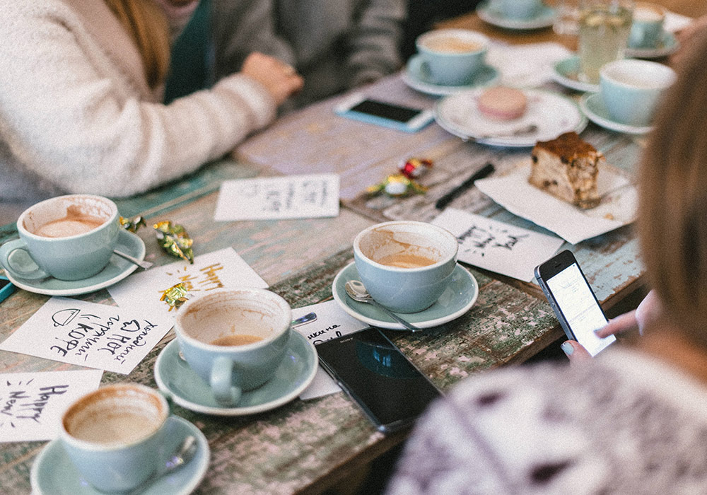 een picknicktafel met kopjes koffie en een groep mensen eromheen