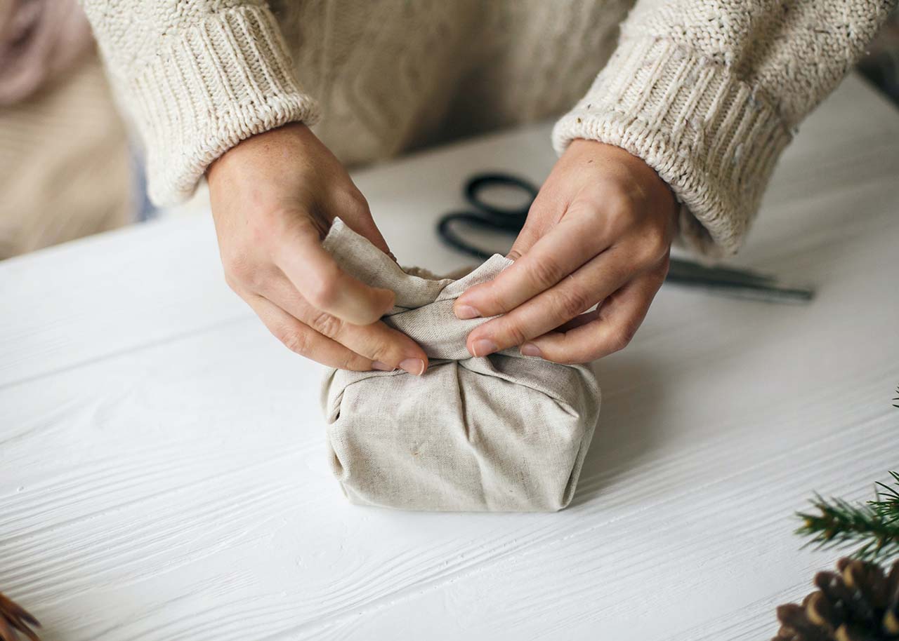 Duurzame kerstcadeaus - handen van een vrouw die een kerstcadeautje inpakt in linnen