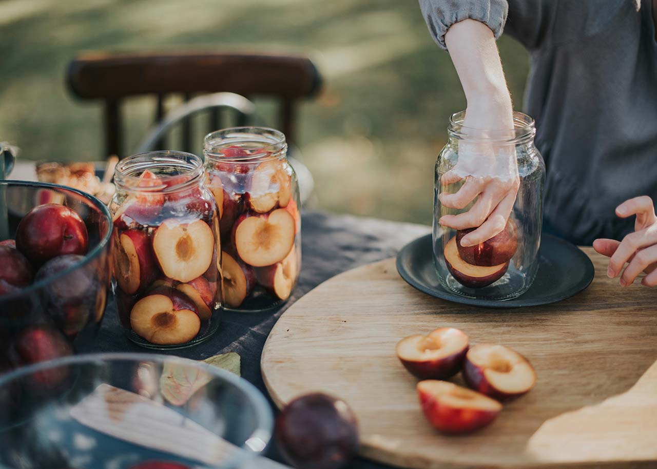 een vrouw die fruit in glazen potten stopt - homemade